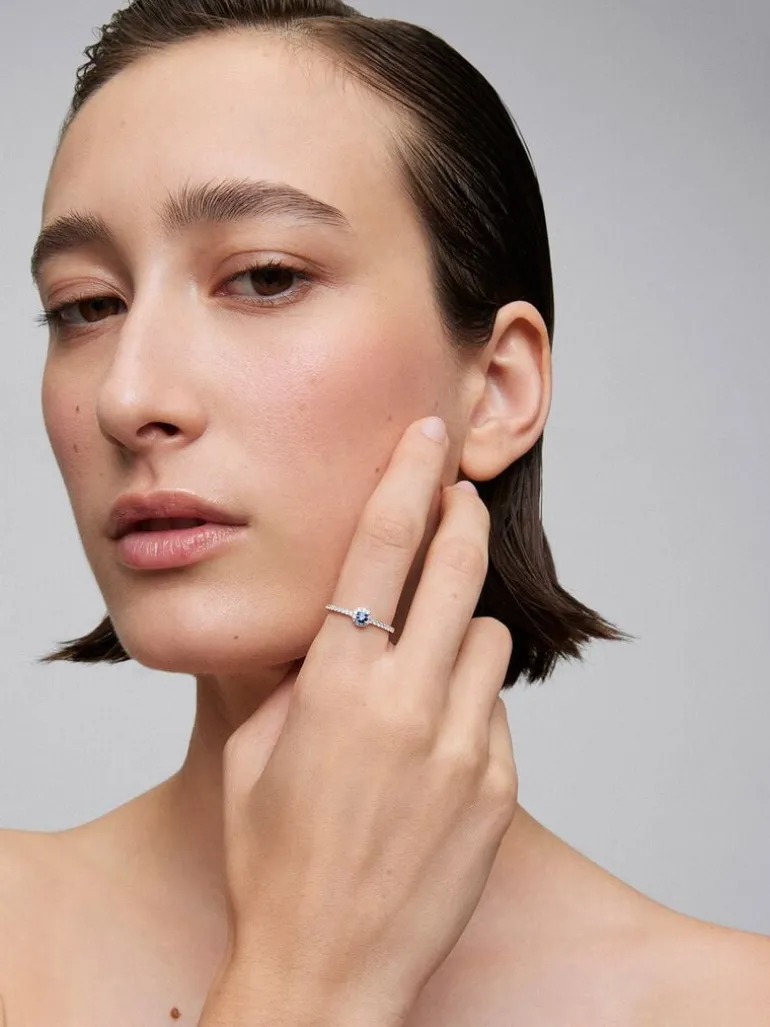 Anillo de oro blanco de 18K con zafiro azul en talla brillante de 0,15 cts y orla y brazo de 28 diamantes en talla brillante con un total de 0,2 cts