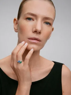 Anillo tú y yo de oro blanco de 18K con un zafiro azul intenso en talla pera de 1,49 cts, una esmeralda verde en talla pera de 1,04 cts y 14 diamantes en talla brillante con un total de 0,64 cts