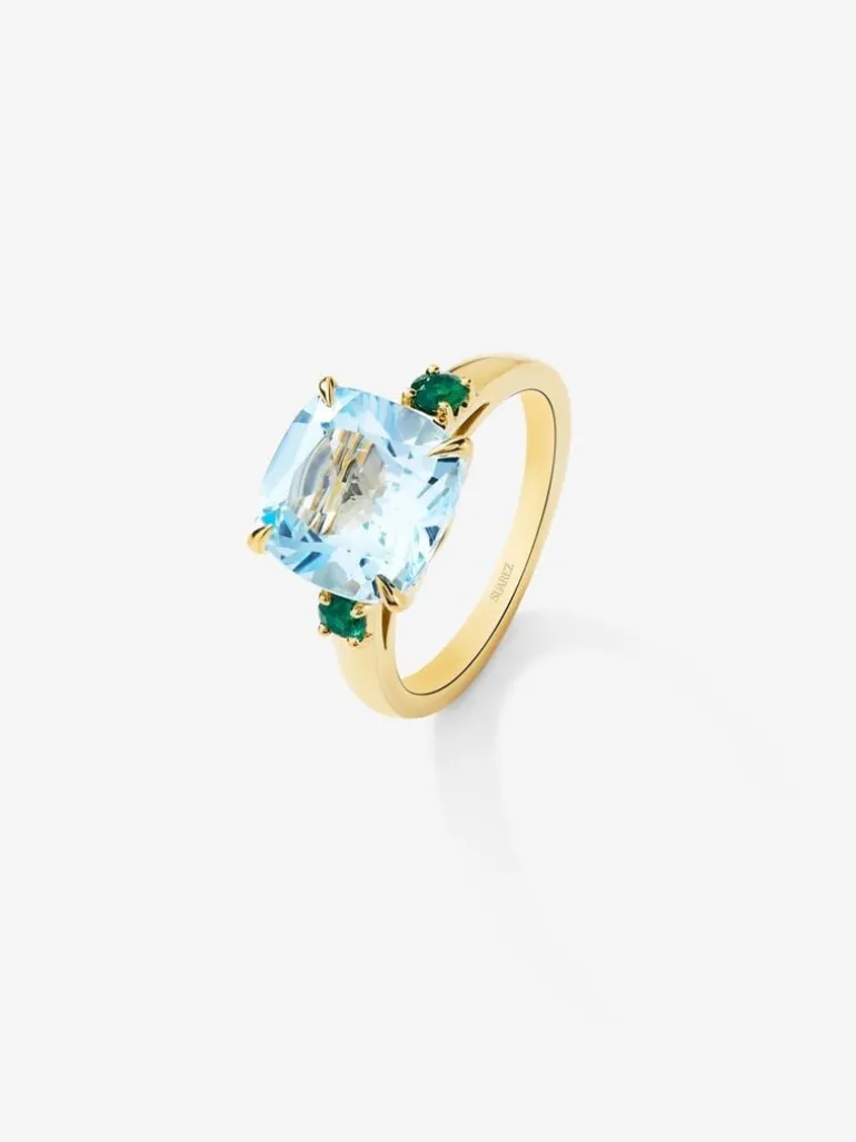 Anillo tresillo de oro amarillo de 18K con topacio azul sky en talla cushion de 4,88 cts y 2 esmeraldas verdes en talla brillante