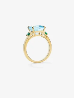 Anillo tresillo de oro amarillo de 18K con topacio azul sky en talla cushion de 4,88 cts y 2 esmeraldas verdes en talla brillante