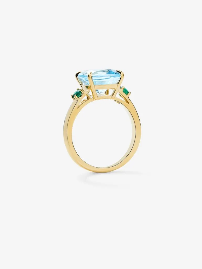 Anillo tresillo de oro amarillo de 18K con topacio azul sky en talla cushion de 4,88 cts y 2 esmeraldas verdes en talla brillante