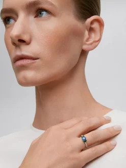 Anillo tresillo de oro blanco de 18K con zafiro azul en talla oval de 0,72 cts, 2 esmeraldas verdes en talla oval con un total de 0,36 cts y 16 diamantes en talla brillante con un total de 0,14 cts